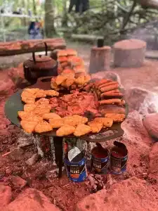 A fire with a large circular cooking surface containing hash browns, bacon and sausages
