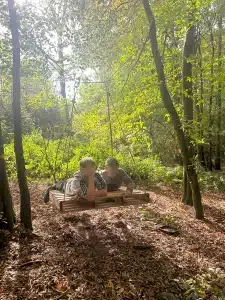 Two boys lying on a pallet that is suspended in the air by ropes connected to trees