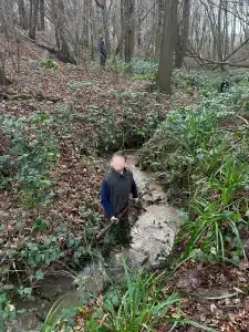 A boy stood in a stream holding a stick