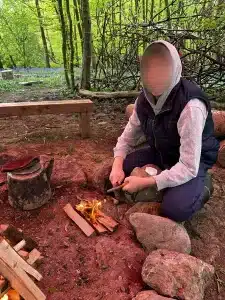 A boy crouched down lighting a fire