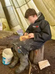 A boy sat on a log whittling wood