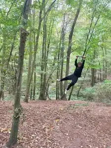 A boy swinging on a rope in the woods holding onto a wooden slat