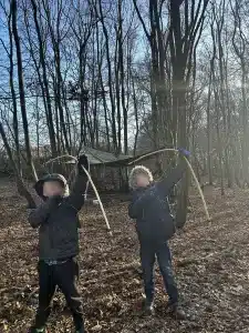 Two boys pulling back the string on bows to fire an arrow in the woods