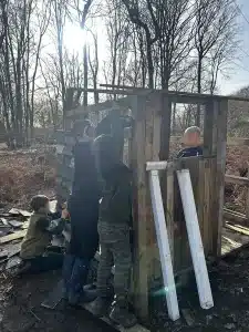 Four boys helping each other to construct a wooden hut in the woods