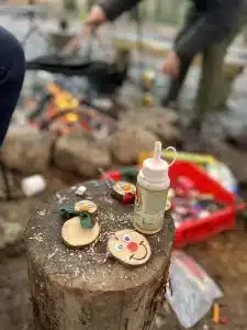 Some smiley faces made out of small circular pieces of wood and a pot of glue sat on a log