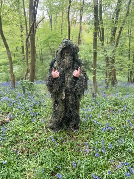 A man wearing a ghillie suit in the woods