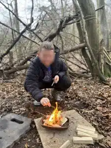 A boy nursing an open fire in the woods