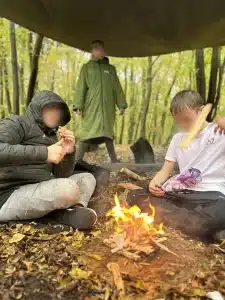 Two boys sat in front of an open fire in the woods