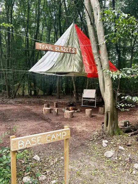 Base Camp at Trail Blazers showing a clearing in the woods with logs for stools and a tarpaulin covering the seating area