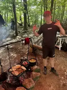 a boy posing for a photo as he stands next to an open fire where food is cooking