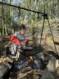 A boy tending to some bacon in a pan over an open fire