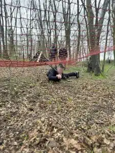A boy lying on the floor army crawling underneath a red net
