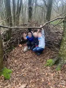 Three boys crouched on the floor in the woods with their arms raised