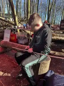 A boy sat on a log whittling some wood