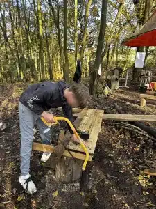 A boy sawing a plank of wood at a makeshift bench in the woods