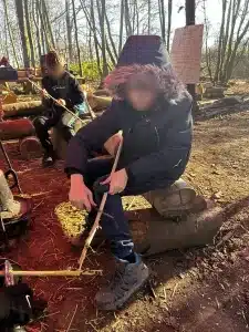 A boy sat on a log whittling some wood