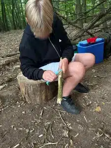A boy sat on a log whittling some wood
