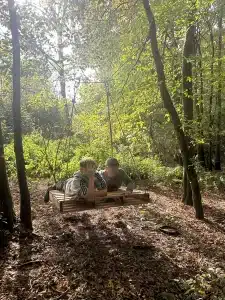 Two boys lying on a pallet that is suspended in the air by ropes connected to trees