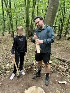 A Trail Blazers staff member explaining to a boy how to chop a log with an axe